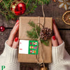 A brown gift box tied with twine and green pine sprigs, featuring Merry Christmas tags.