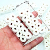 Une main tient un paquet transparent de rouleaux miniatures de papier toilette blanc pour décoration de maison de poupée.