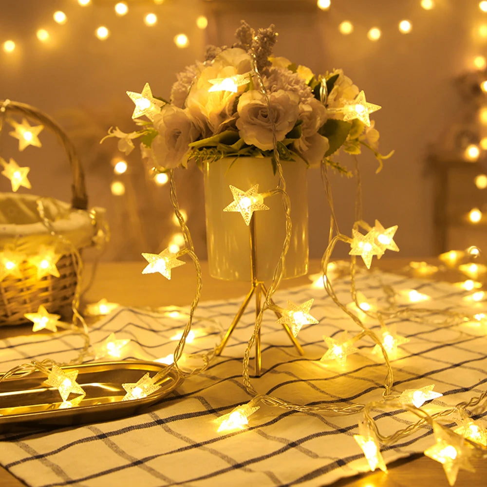 A bouquet of light-colored roses displayed in a vase surrounded by glowing LED star fairy lights on a checkered cloth.
