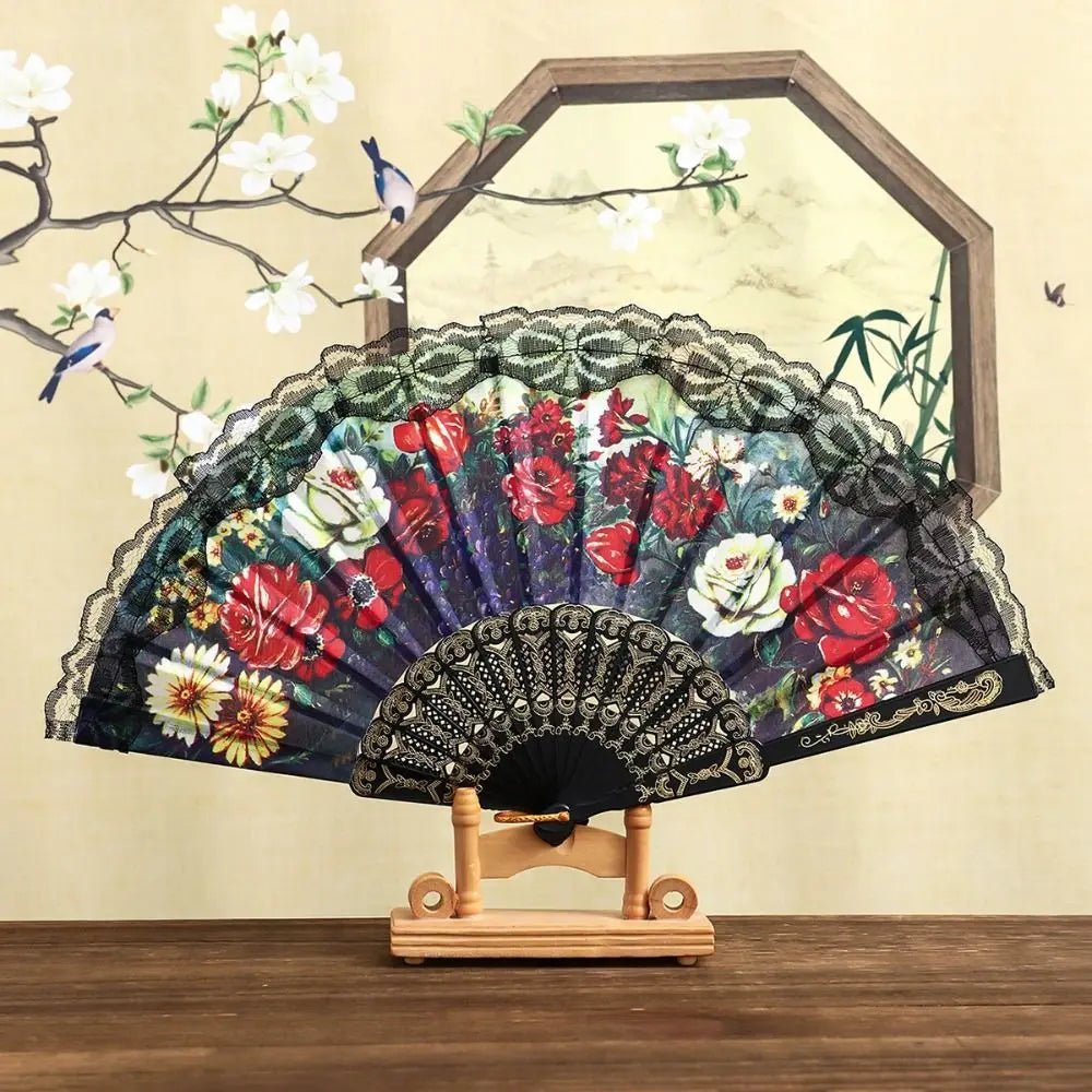 A Spanish style folding lace trim handheld fan with dark fabric and floral patterns displayed in front of a framed artwork.