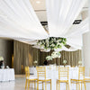 White draped fabric ceiling and background curtains with gold chairs set up for an event.