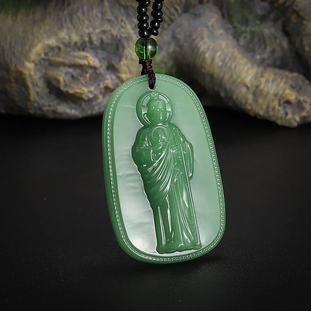 A green jade pendant featuring a statue of Saint Jude Thaddeus on a dark cord.