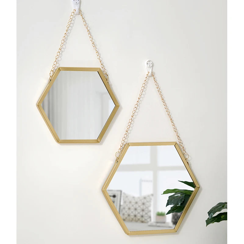 A gold-framed hexagon decorative wall mirror hanging by a delicate chain.