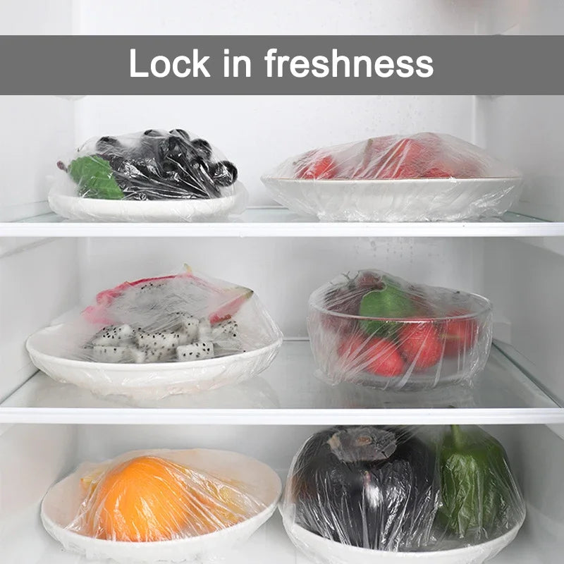 Various fresh foods like strawberries, herbs, and vegetables are stored in clear reusable cling film in white bowls.
