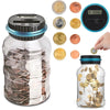 A clear glass piggy bank filled with coins, next to various gold and copper coins and a digital coin counting device.