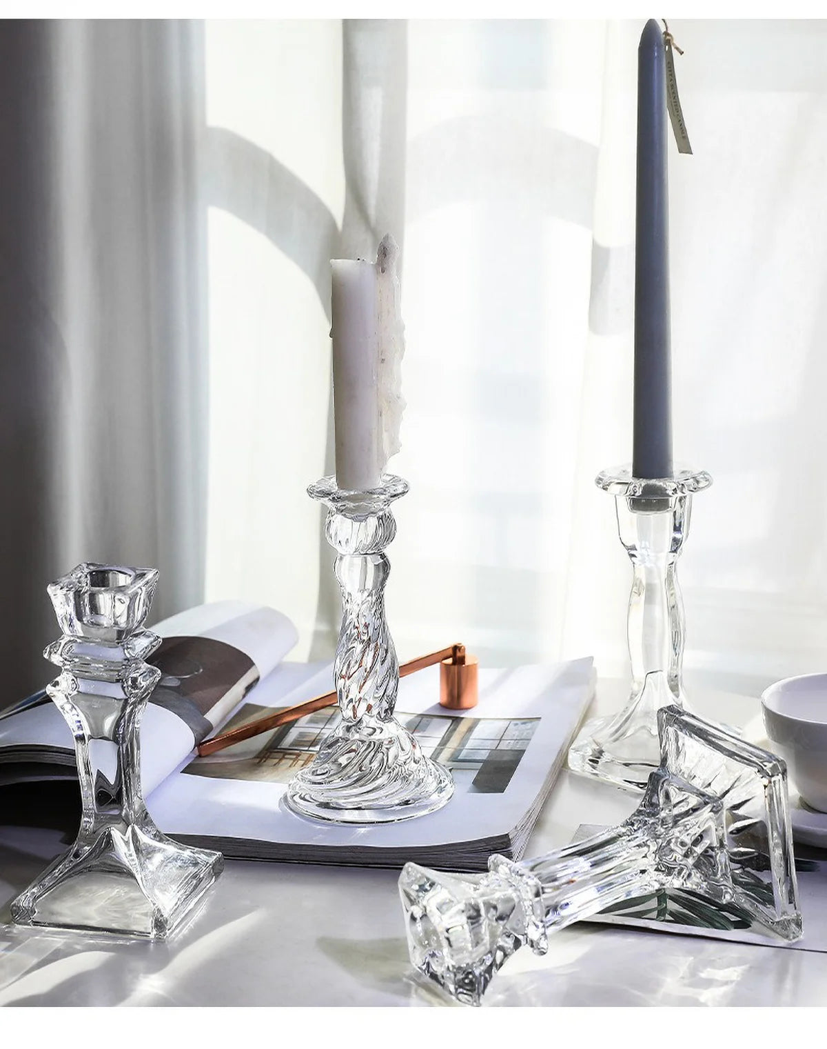Elegant clear glass pillar candle holder with a white candle on a light gray surface.