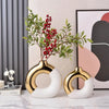 Two gold and white ceramic flower vases with green leaves and red berries displayed against a neutral background.