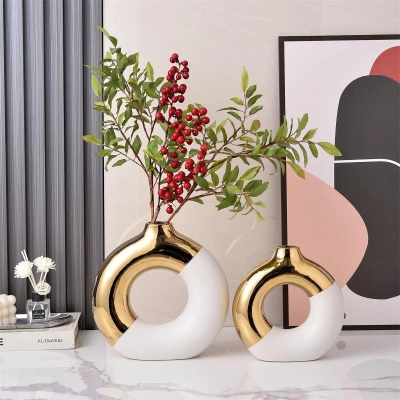 Two gold and white ceramic flower vases with green leaves and red berries displayed against a neutral background.