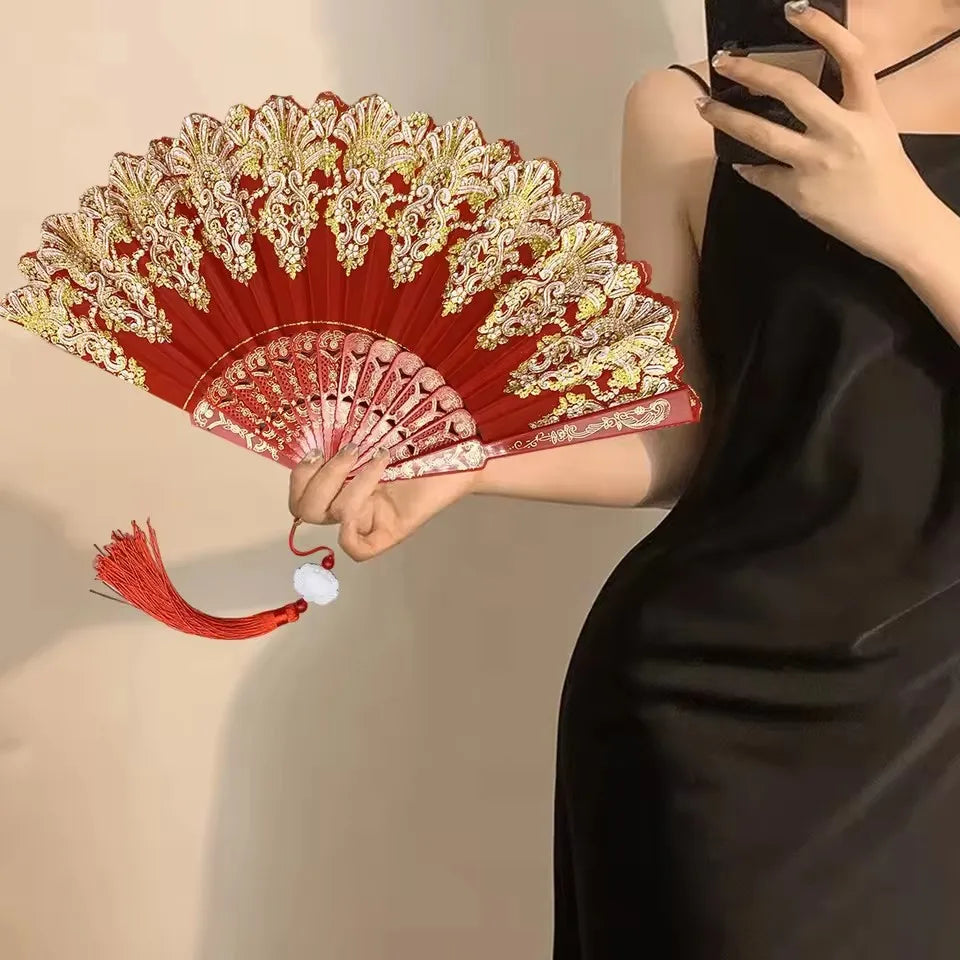 A woman holds an elegant red and gold folding fan with traditional Chinese design against a light background.