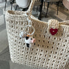 A handmade crochet cow keychain with a white and black cow figure and a red heart charm