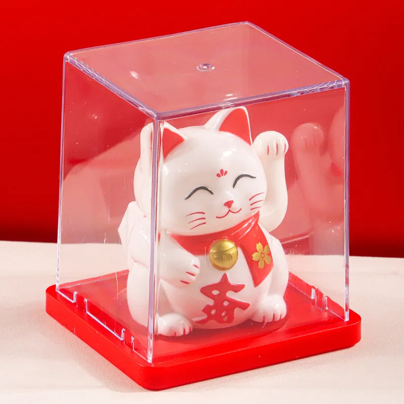 A white lucky cat figurine with red accents is displayed inside a clear acrylic box on a red base.
