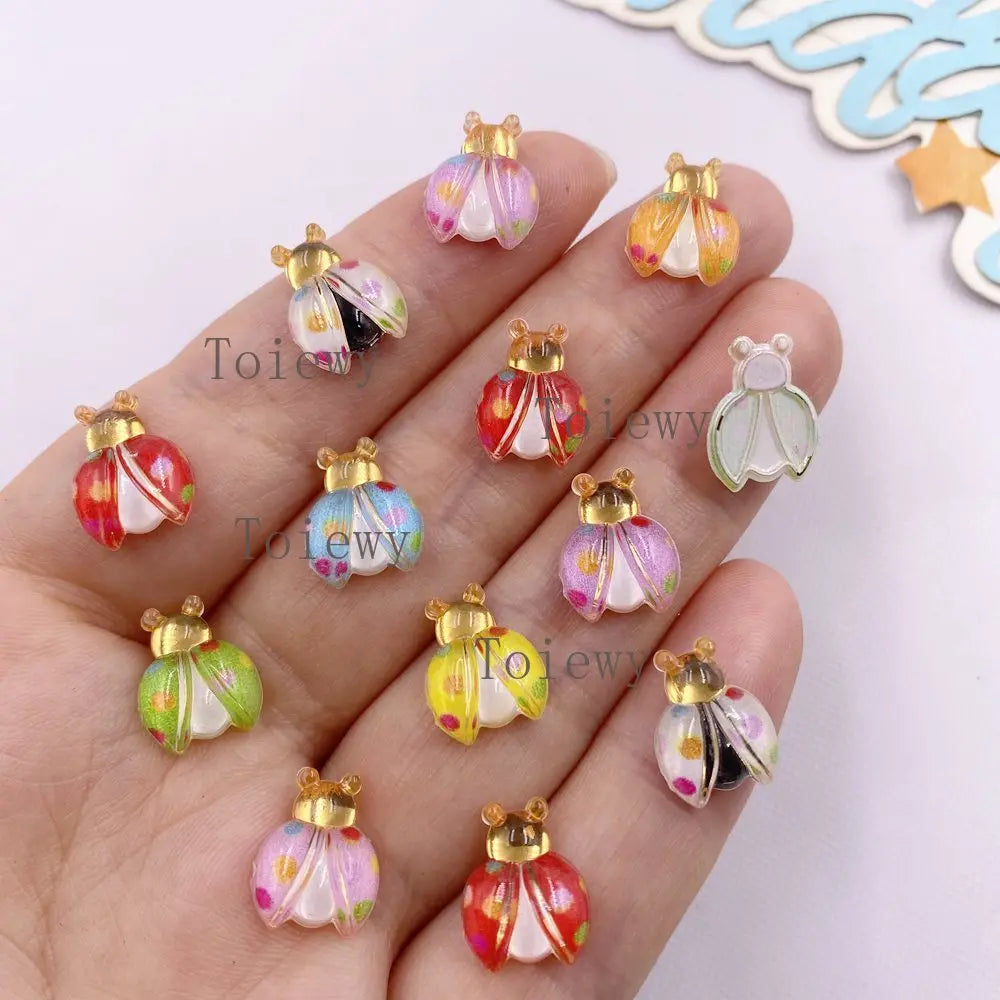 A hand holds several colorful resin beetle rhinestone appliques for DIY crafts.