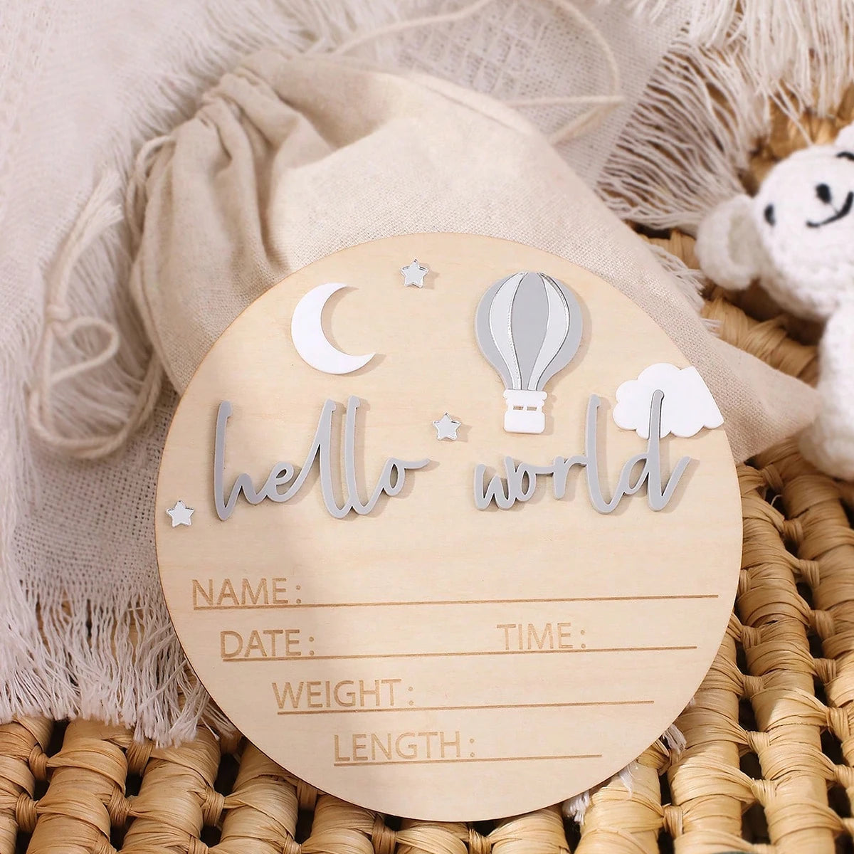 A wooden birth announcement sign with the text hello world and fields for name date time weight and length is placed on a bei