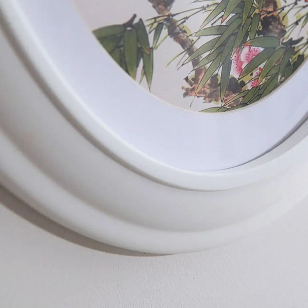 A white oval picture frame with a natural green and pink foliage pattern is shown from above.