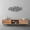 A black geometric metal wall art sculpture with intersecting lines mounted on a gray wall above a light wood shelf.