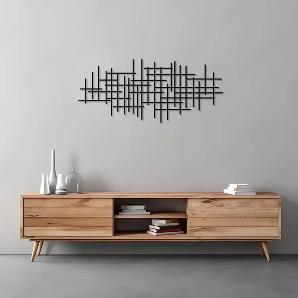 A black geometric metal wall art sculpture with intersecting lines mounted on a gray wall above a light wood shelf.