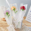 A bouquet of handmade crochet tulips in various colors, including purple and red, displayed in a clear wire basket.