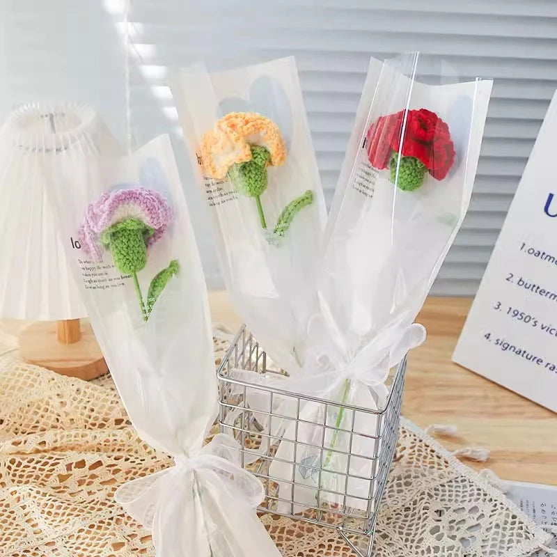 A bouquet of handmade crochet tulips in various colors, including purple and red, displayed in a clear wire basket.
