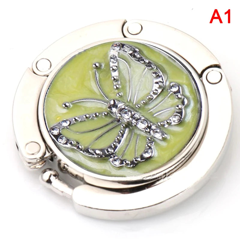 Silver foldable handbag hook designed for securing bags on tables and desks.