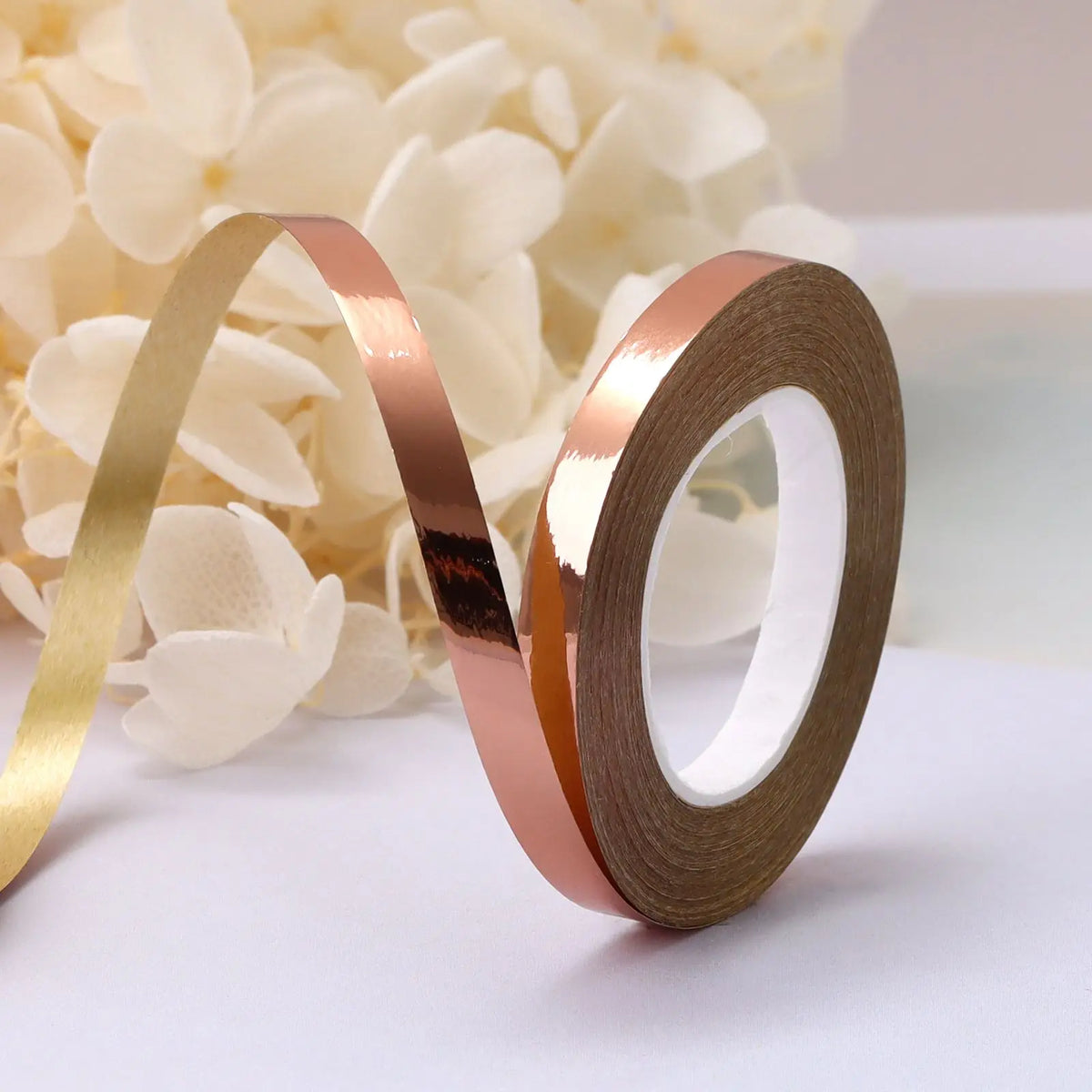 Roll of rose gold satin balloon ribbon unwinding on a white surface