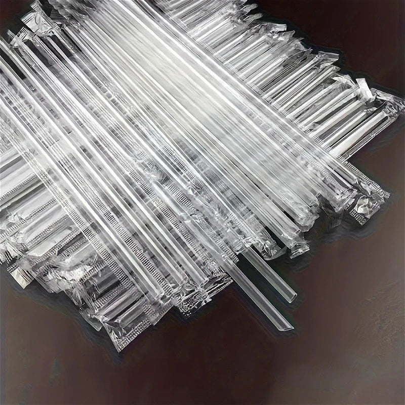 A pile of clear disposable drinking straws laid diagonally on a dark surface.
