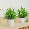 A set of four small artificial bonsai plants in green foliage potted in white ceramic containers on a wooden table.