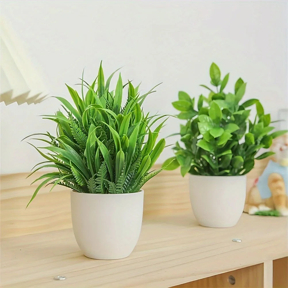 A set of four small artificial bonsai plants in green foliage potted in white ceramic containers on a wooden table.