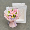 A bouquet of pink and yellow handmade crochet flowers wrapped in pink paper, presented in a white paper bag.