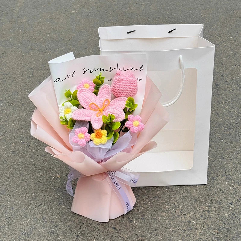 A bouquet of pink and yellow handmade crochet flowers wrapped in pink paper, presented in a white paper bag.