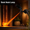 A book nook lamp featuring a dragon silhouette with glowing orange flame light illuminating books.