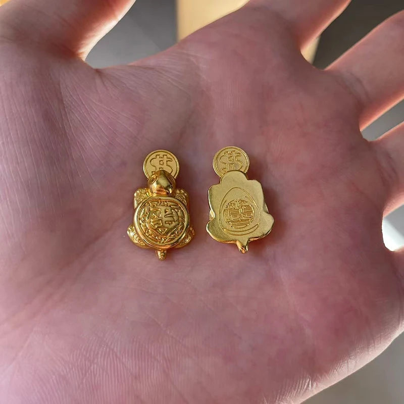 Two golden tortoise figurines for wealth luck home decor resting on a person's hand.