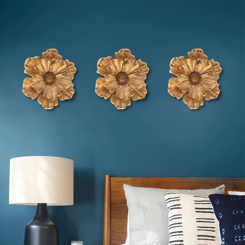 Three textured gold flower wall art pieces displayed on a dark blue wall above a wooden bed.