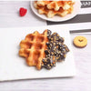 A white plate features a waffle and chocolate drizzle on a white rectangular plate with a red raspberry nearby.