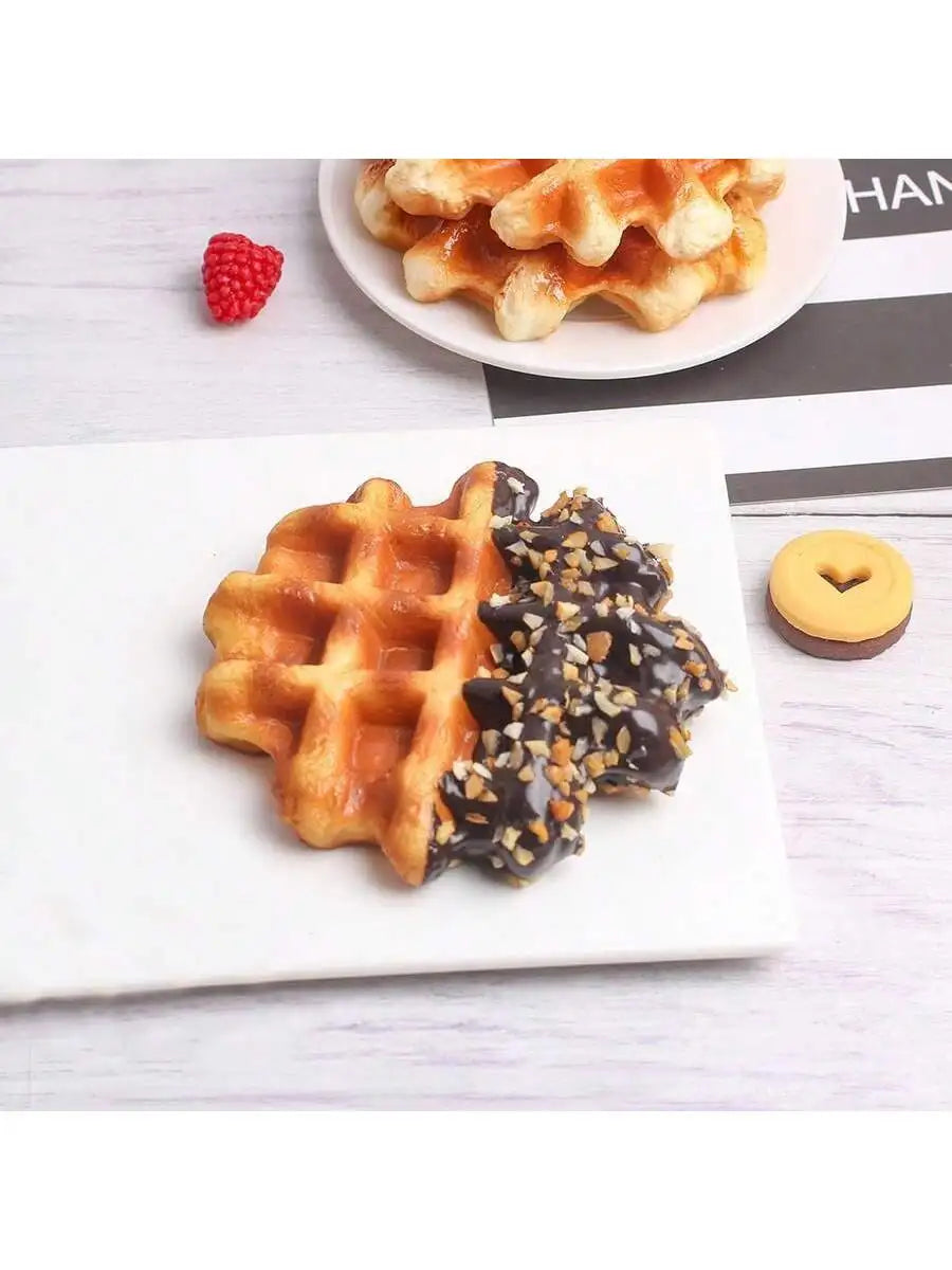 A white plate features a waffle and chocolate drizzle on a white rectangular plate with a red raspberry nearby.