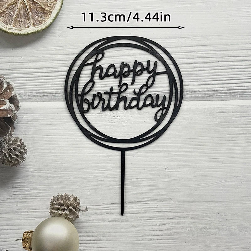 Black acrylic birthday cake topper with gold lettering on a white wooden background