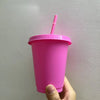 A hand holds a bright pink plastic cold cup with a pink lid and straw against a white wall.
