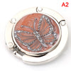 A silver foldable handbag hook with a butterfly design on a pink background.