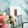 A white wall-mounted organizer with phone holder and charging dock is displayed against a light blue marbled background.