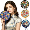 A woman wearing a silk top holds a floral foldable pocket fan with blue and orange accents.