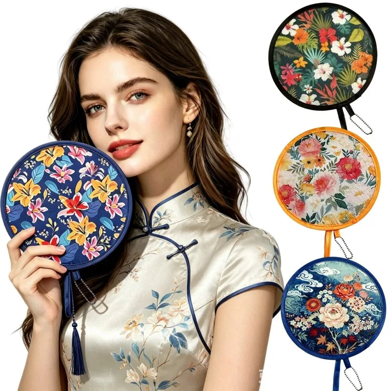 A woman wearing a silk top holds a floral foldable pocket fan with blue and orange accents.