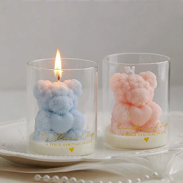 A pink rose bear scented soy wax candle in a glass cup set on a white plate.