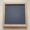 A rectangular wooden letter message board with a dark gray slatted surface and a light wood frame.