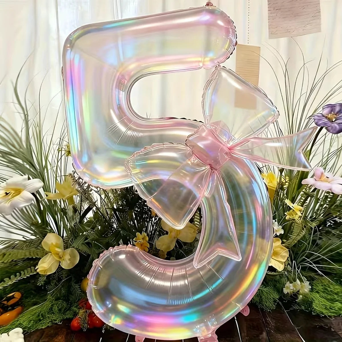 A large, iridescent, transparent number balloon shaped like the number 5 is displayed in a festive floral arrangement.