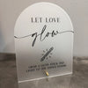 A white acrylic sign with black script that reads Let Love glow and features an illustration of a glow stick.
