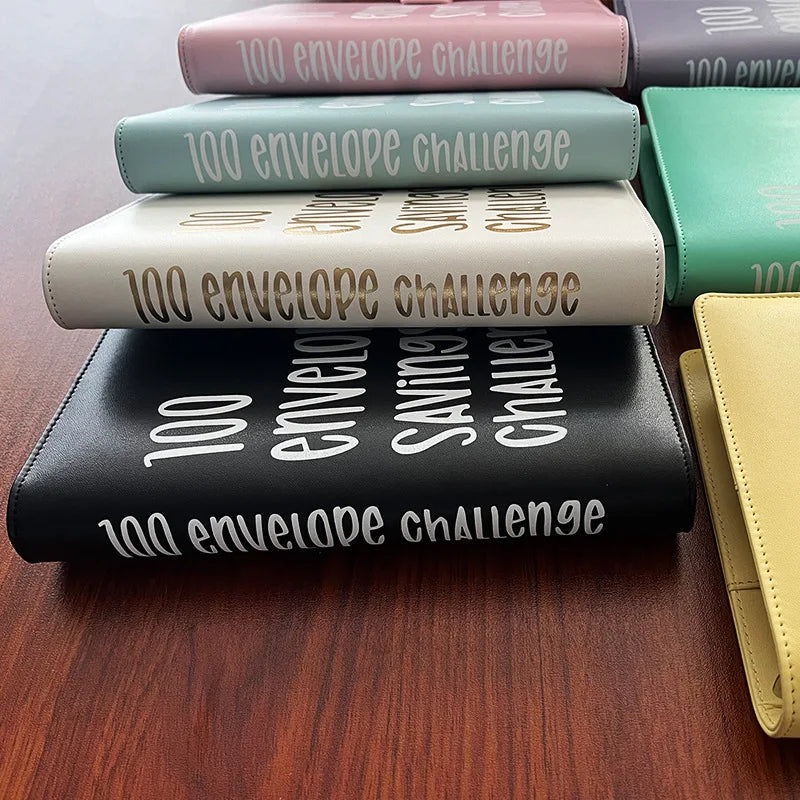 A stack of 100 Envelope Challenge binders in various pastel and dark colors, showing the envelopes on top.