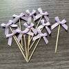 A set of purple ribbon bows on wooden sticks used as cupcake toppers for parties.