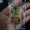 A gold credit suisse bullion ingot in a clear plastic protective sleeve being held in a hand.