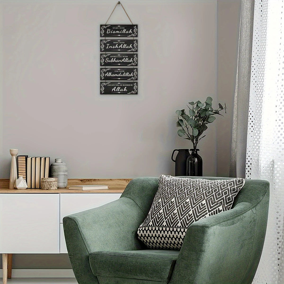 A green armchair in a room with a framed Islamic calligraphy sign on the wall.