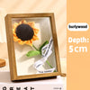 A wooden shadow box frame containing a textured orange flower with a black center and a green stem.