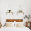 A bedroom setting featuring two handmade macrame wood wall shelves with tassels above a white bed.